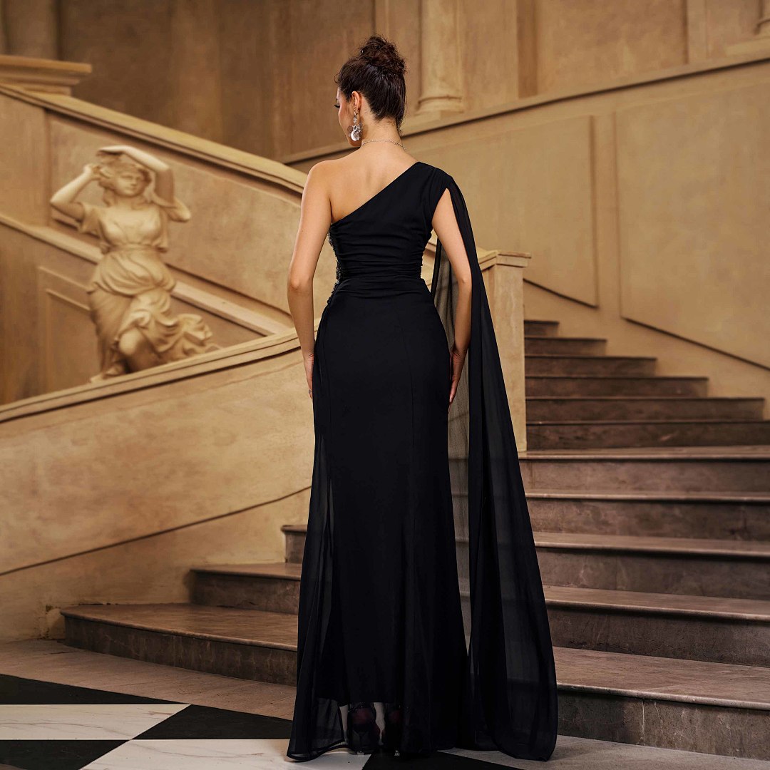 Back view of black one-shoulder evening gown with beaded detail and long tulle drape