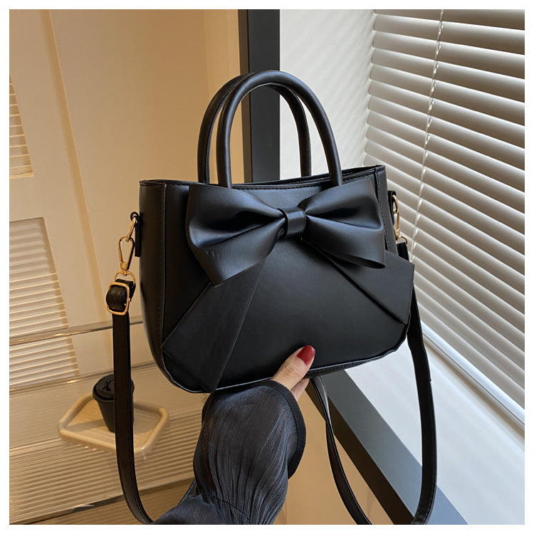 Black bow-trimmed small square handbag with wide bow front and shoulder strap