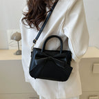 Black bow-trimmed small square handbag with top handle and crossbody strap