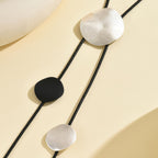 Disc tassel necklace with black cord and round matte pendants in white and black