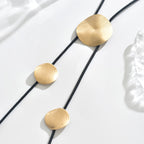 Gold disc tassel necklace with black cord and several round metal pendants