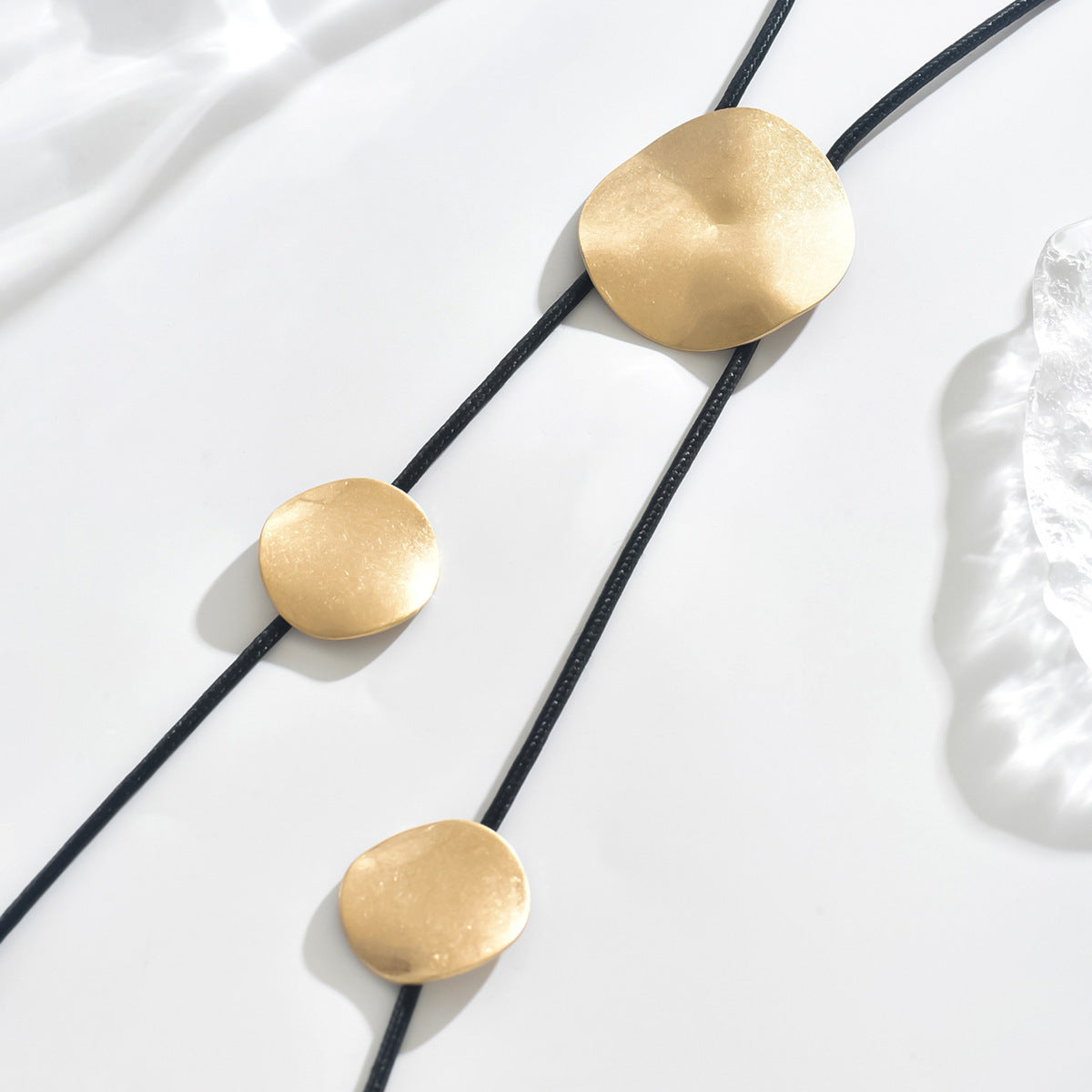 Gold disc tassel necklace with black cord and several round metal pendants
