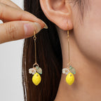 Gold-tone lemon drop earrings with green leaf and white flower charms on dangling hooks