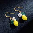 Pair of lemon drop earrings with yellow lemon charms, green leaves, and white floral accents