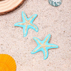 Starfish stud earrings with two blue enamel starfish on sand, orange shell edge