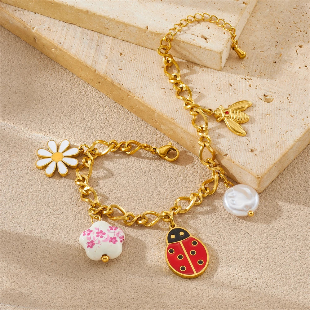 Gold-tone charm bracelet with ladybug pendant, white flower and pearl drops; chained design