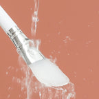 Silicone face mask brush with white silicone head and chrome handle, water droplets visible