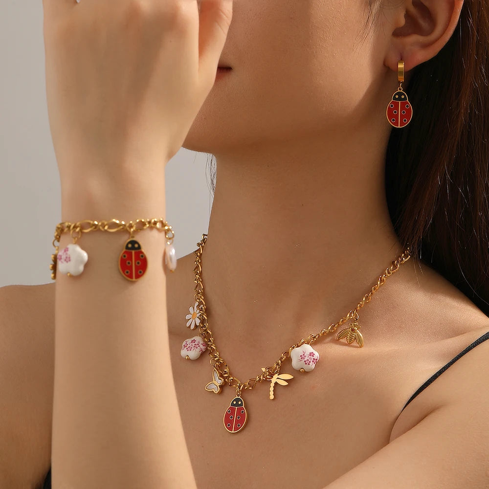 Gold-tone charm necklace with ladybug and flower pendants, plus matching stud earrings and bracelet