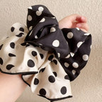 Cotton polka-dot scrunchies in cream and black with white dots, held in hand