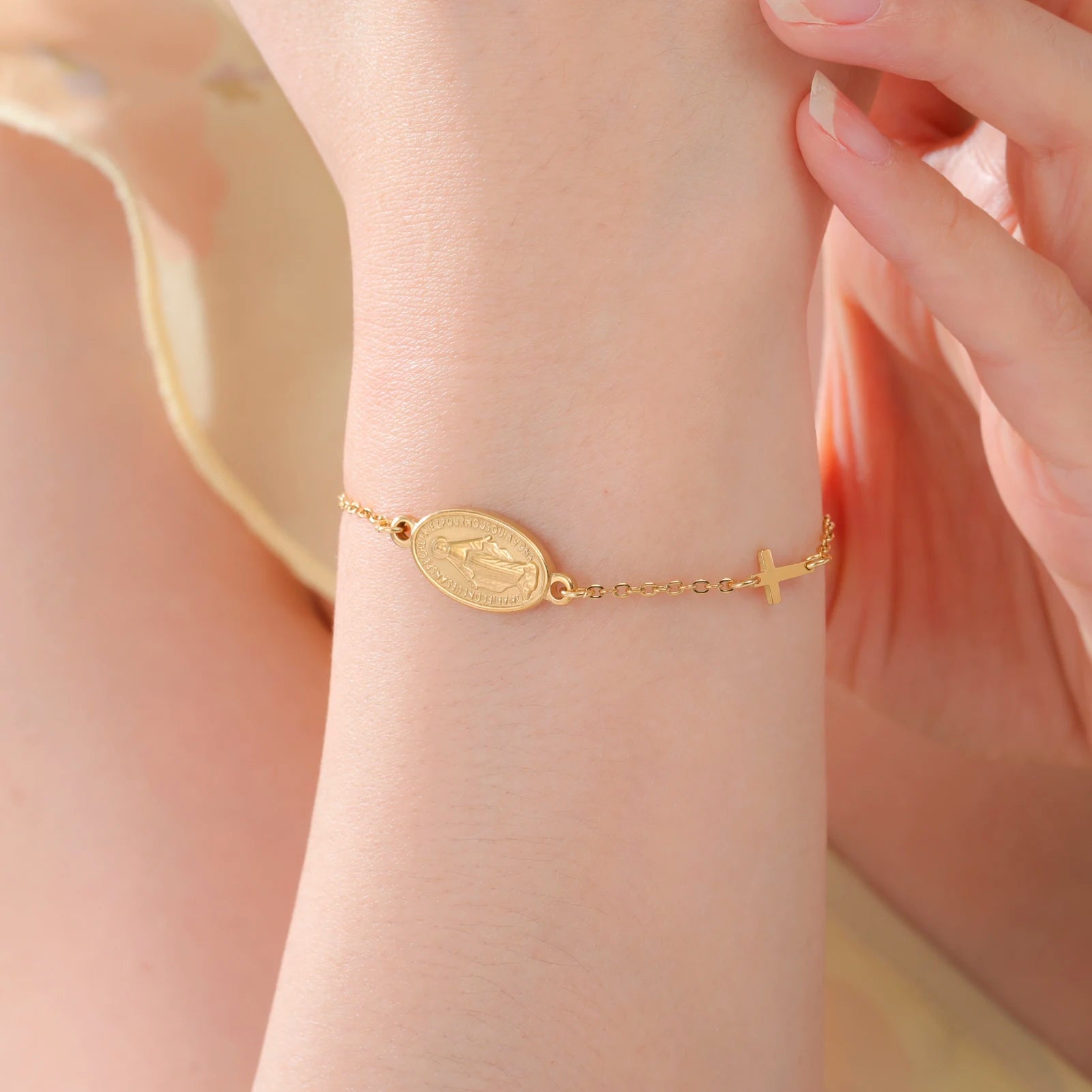 Gold-tone Virgin Mary bracelet with oval pendant and cross charm, worn on wrist