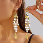 Gold-tone koi charm earrings with blue eye details and white shell-like beads.