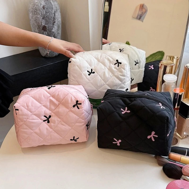 Assorted quilted cosmetic bags in pale pink, white, and black with bow embroidery