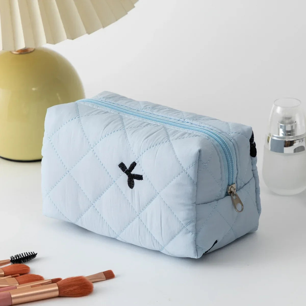 Light blue quilted cosmetic bag with black bow embroidery and zip closure