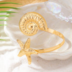 Gold shell-and-starfish arm cuff featuring textured shell disk and raised starfish charm
