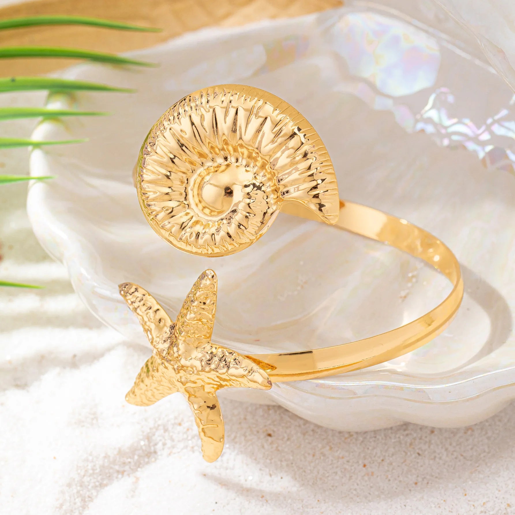 Gold shell-and-starfish arm cuff featuring textured shell disk and raised starfish charm