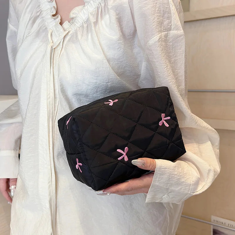 Black quilted cosmetic bag with pink bow embroidery and zip closure