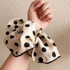 Cream cotton polka-dot scrunchie with black dots, gathered fabric bow held in hand