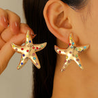 Gold starfish stud earrings with rainbow rhinestones, worn on ears
