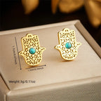Gold-tone hamsa stud earrings with turquoise center on jewelry box