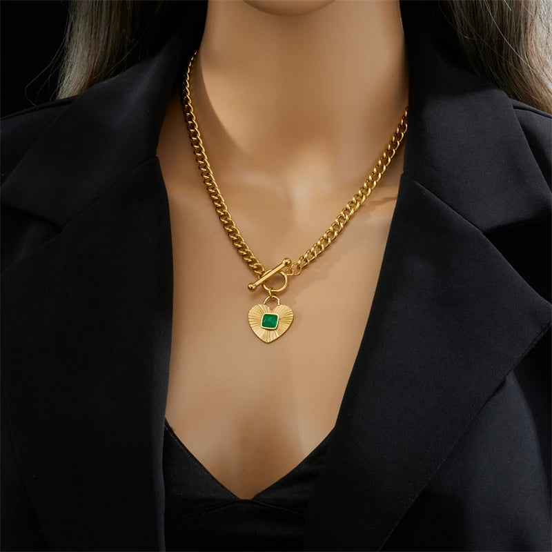 Gold-tone heart pendant necklace on a model’s neckline with green square stone charm
