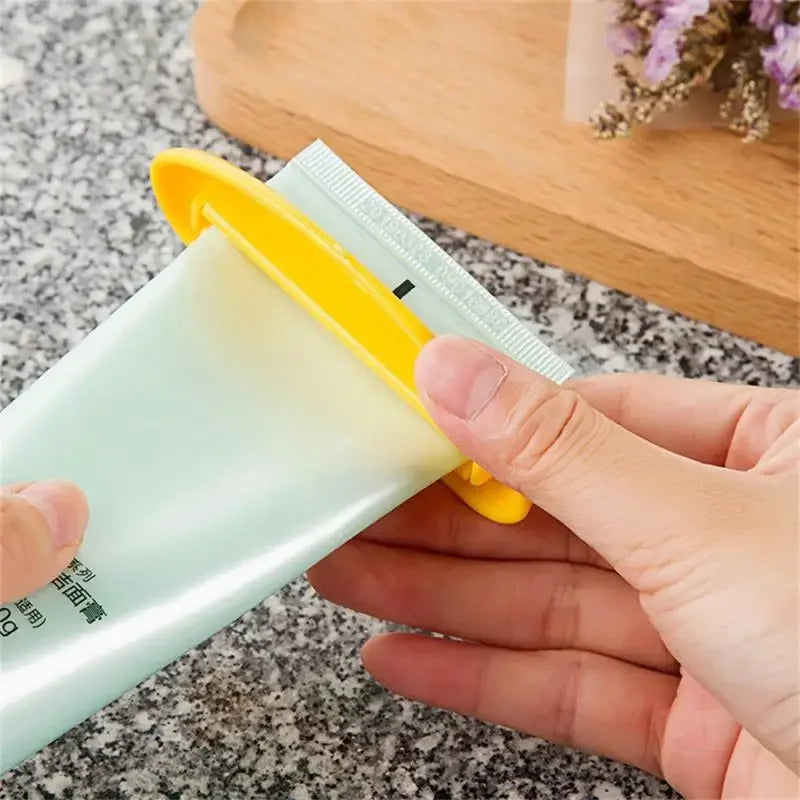 Yellow toothpaste tube squeezer dispenser with metal channel, gripping a tube in hand