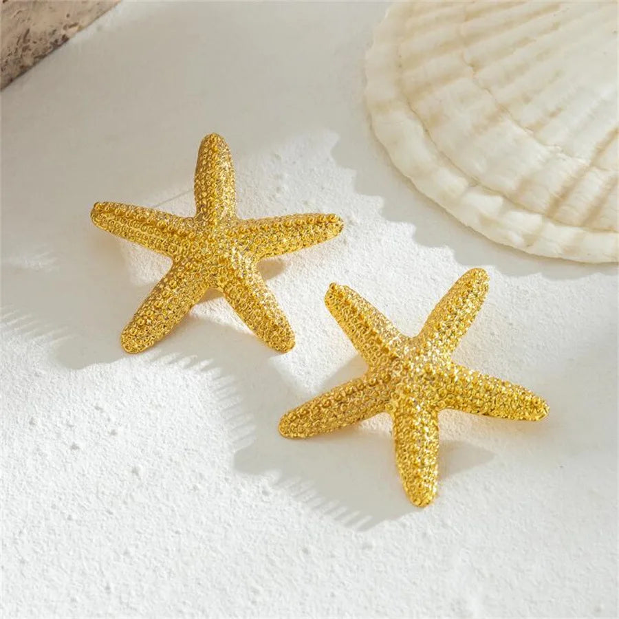 Gold starfish charm on a white surface next to seashell decor.