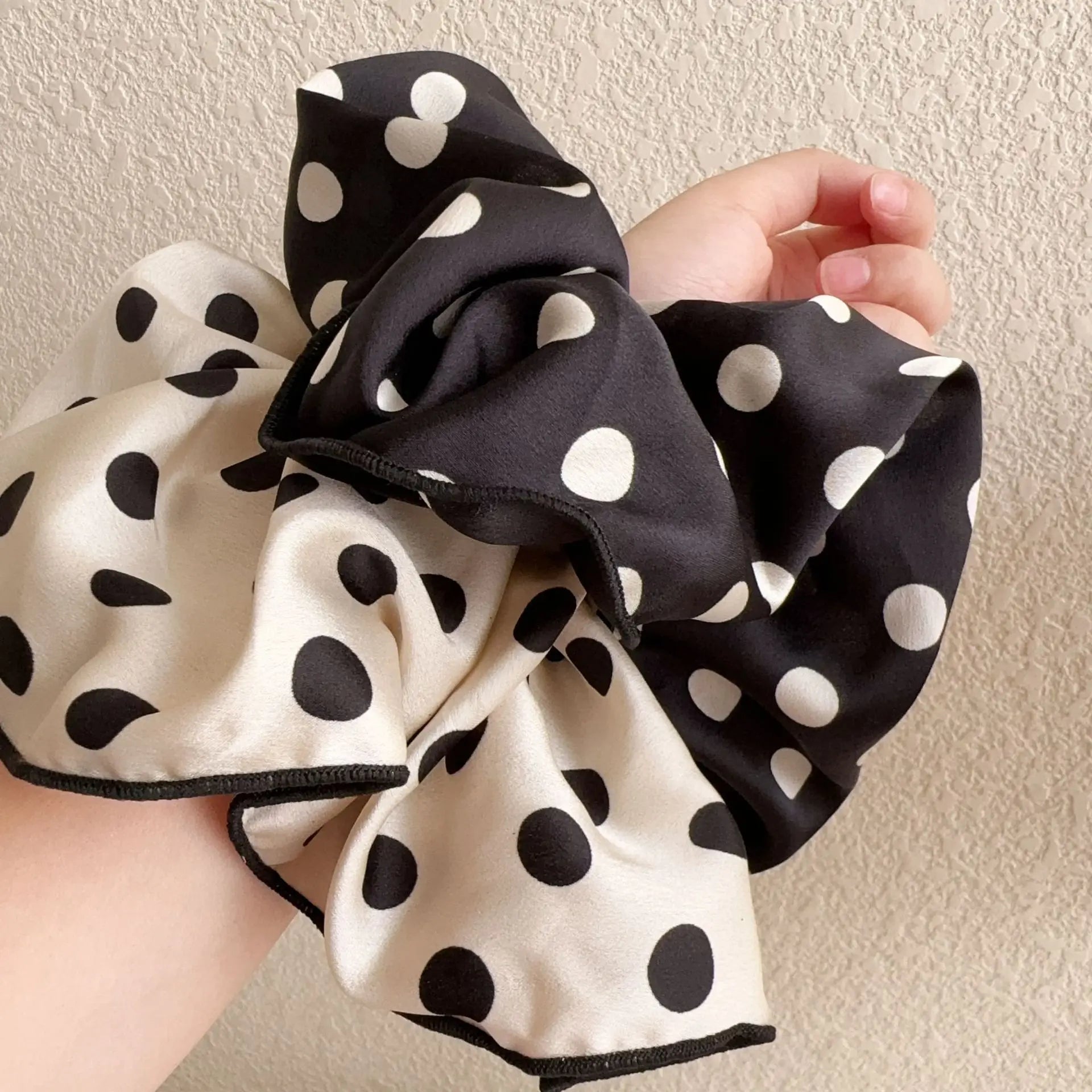 Cotton scrunchies in cream and black polka dots with white dots, held in hand