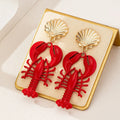 Gold-tone red lobster dangle earrings with scallop shell studs shown side-by-side