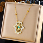 Gold-tone hamsa hand pendant necklace with turquoise center on display box