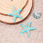 Starfish stud earrings with two blue enamel starfish on sand and shell piece