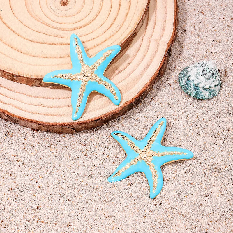 Starfish stud earrings with two blue enamel starfish on sand and shell piece