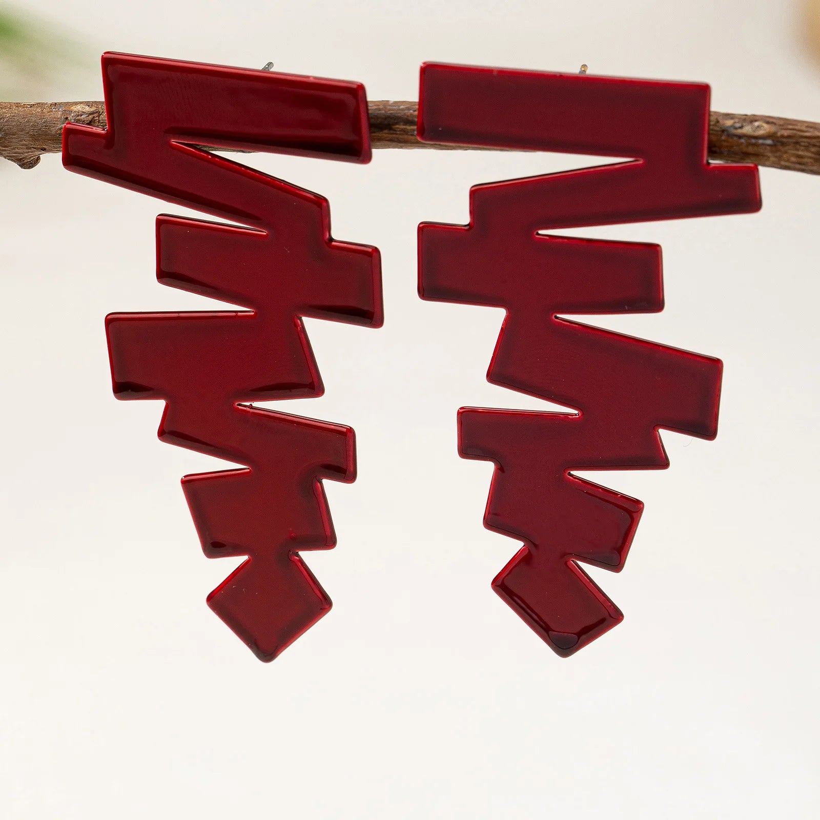 Geometric stud earrings in deep red with layered zigzag shapes on the ear