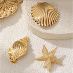 Gold starfish, scallop shell, and clam shell hair clips on a white textured card