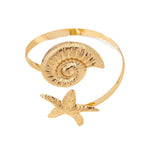 Gold-toned open cuff arm ring with textured shell disk and starfish charm below