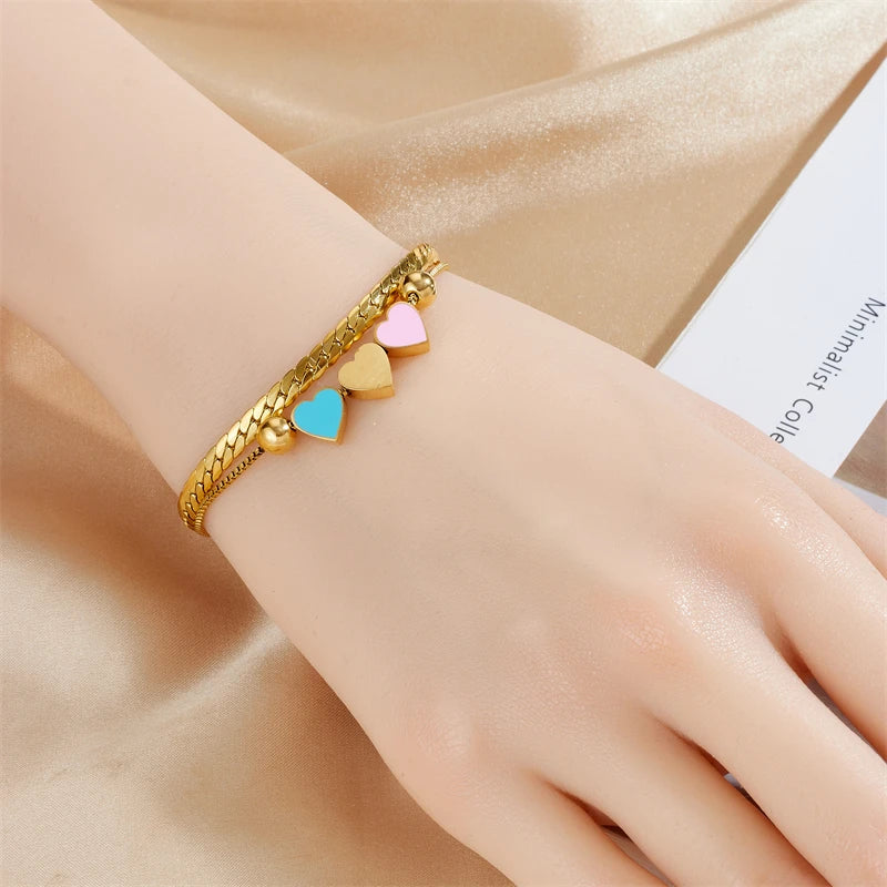 Gold heart charm bracelet with blue, pink, and cream enamel hearts on rope chain