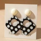 Polka-dot square drop earrings with black discs and white ball tops on a jewelry card