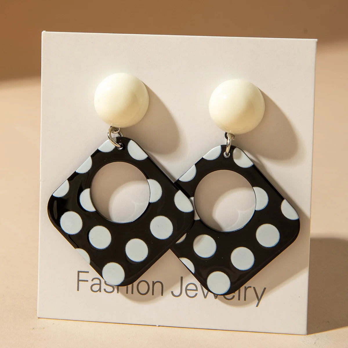 Polka-dot square drop earrings with black discs and white ball tops on a jewelry card