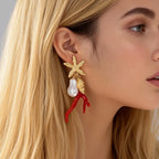 Star-and-figure resin earrings on model ear: red coral drops and white pearl, gold-tone