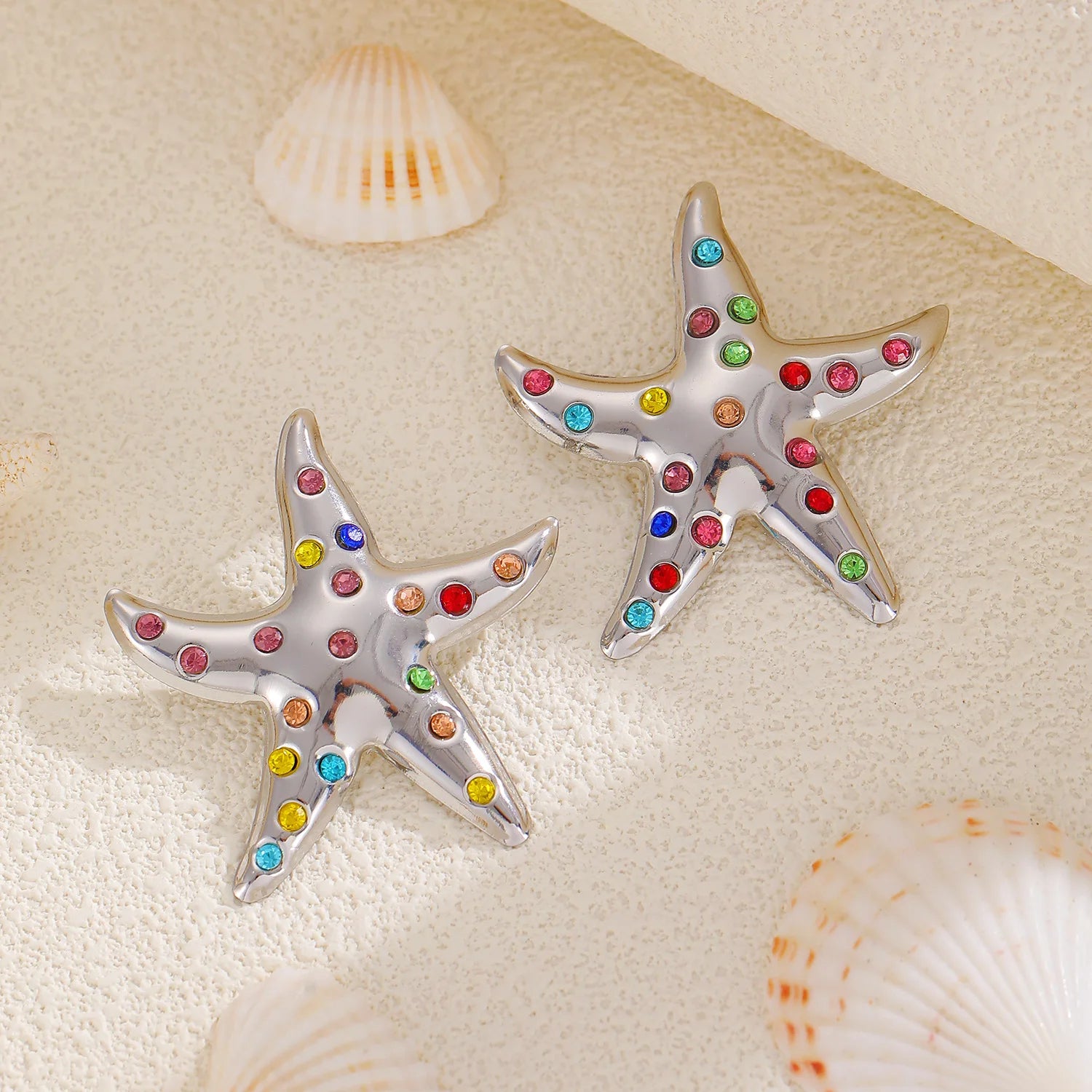 Silver starfish stud earrings with multicolor rhinestones, shown pair on seashells