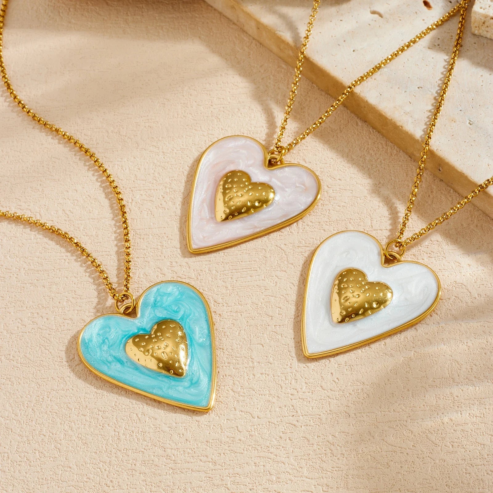 Two enamel heart pendants on gold chains: blue and white with gold inner hearts