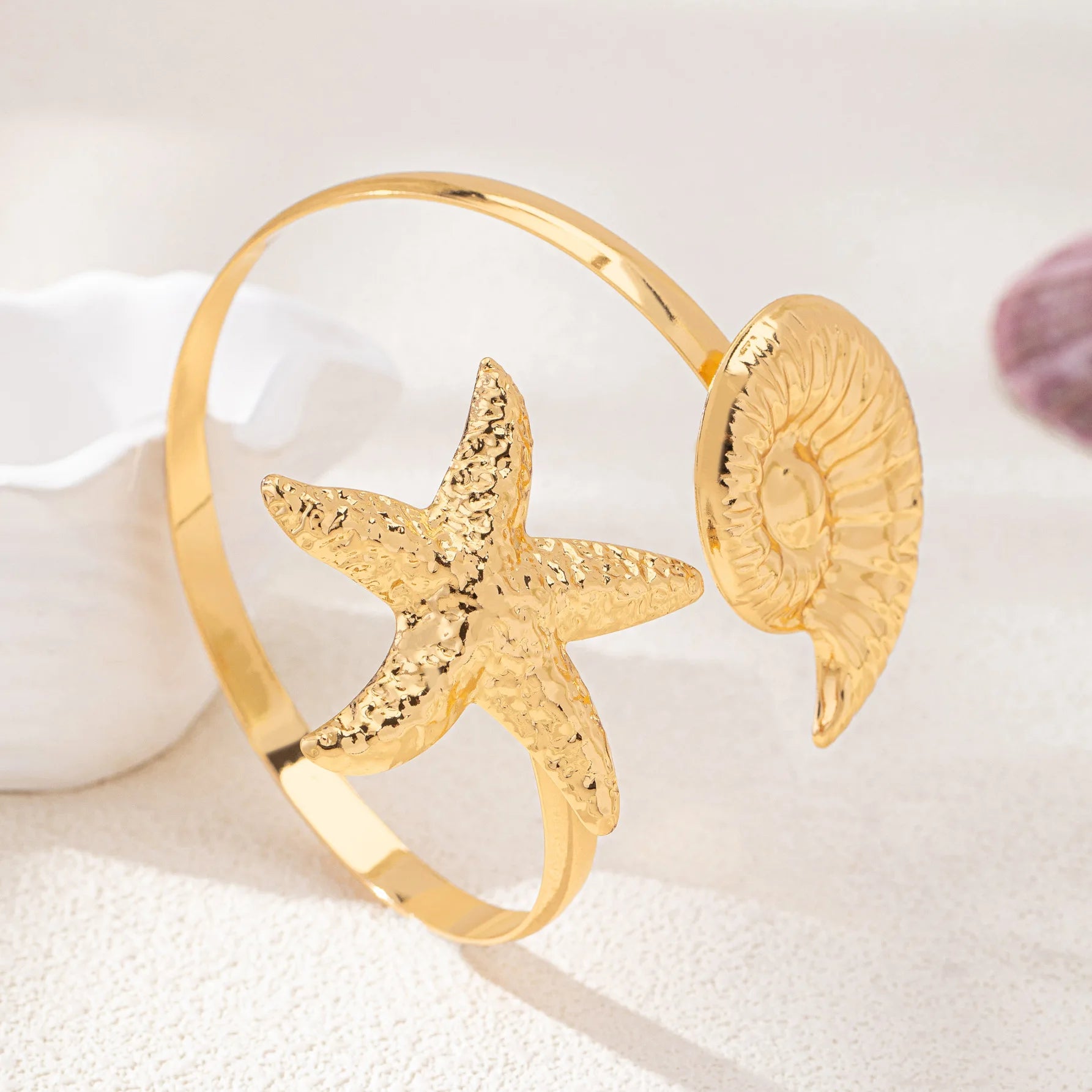 Gold starfish arm cuff with textured starfish and round shell disk centerpiece