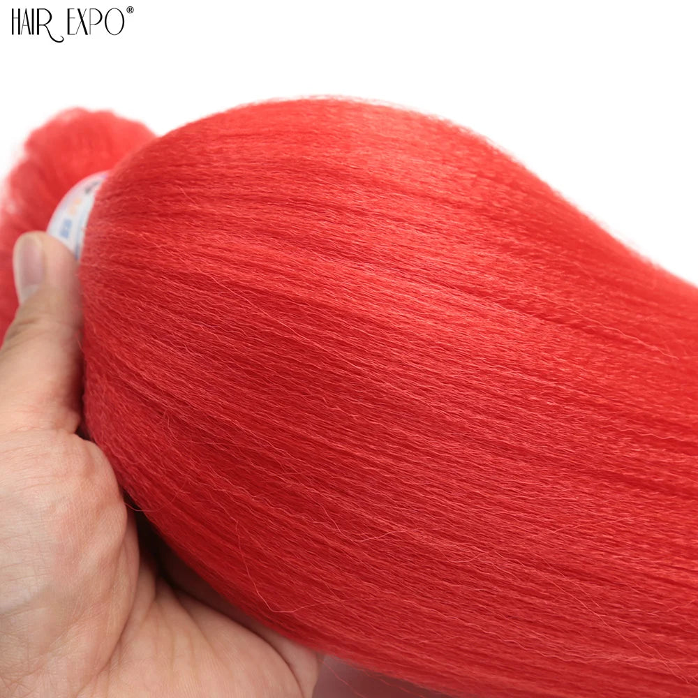 Red synthetic braiding hair extension bundle, held by hand, thick strands