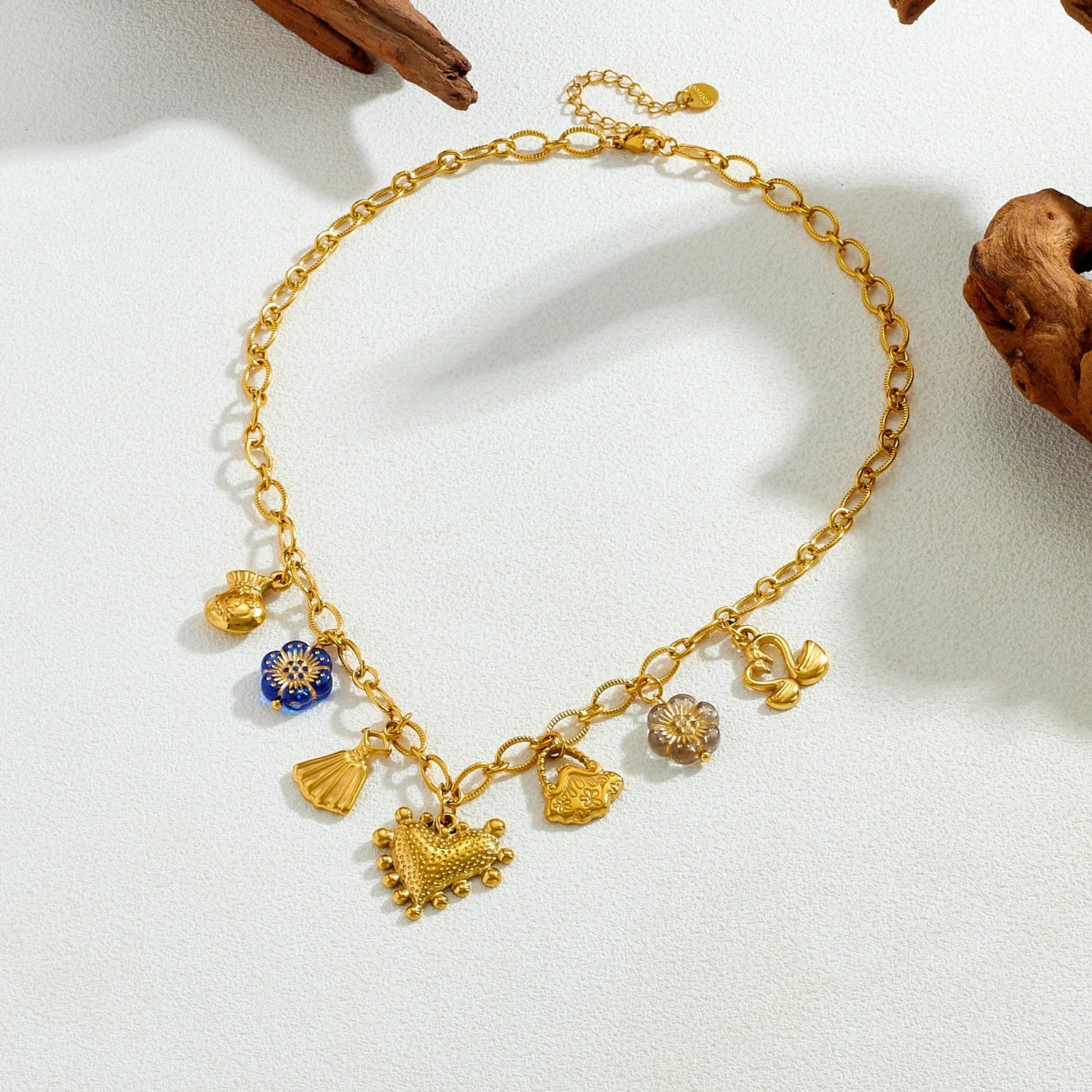 Gold-tone multi-pendant necklace with blue flower charm, tassel, and heart-like centerpiece