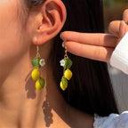 Lemon drop earrings dangling from gold hooks with yellow lemons and green leaf charms