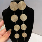 Gold-tone woven disc dangle earrings on black card, four-circle fringe drops