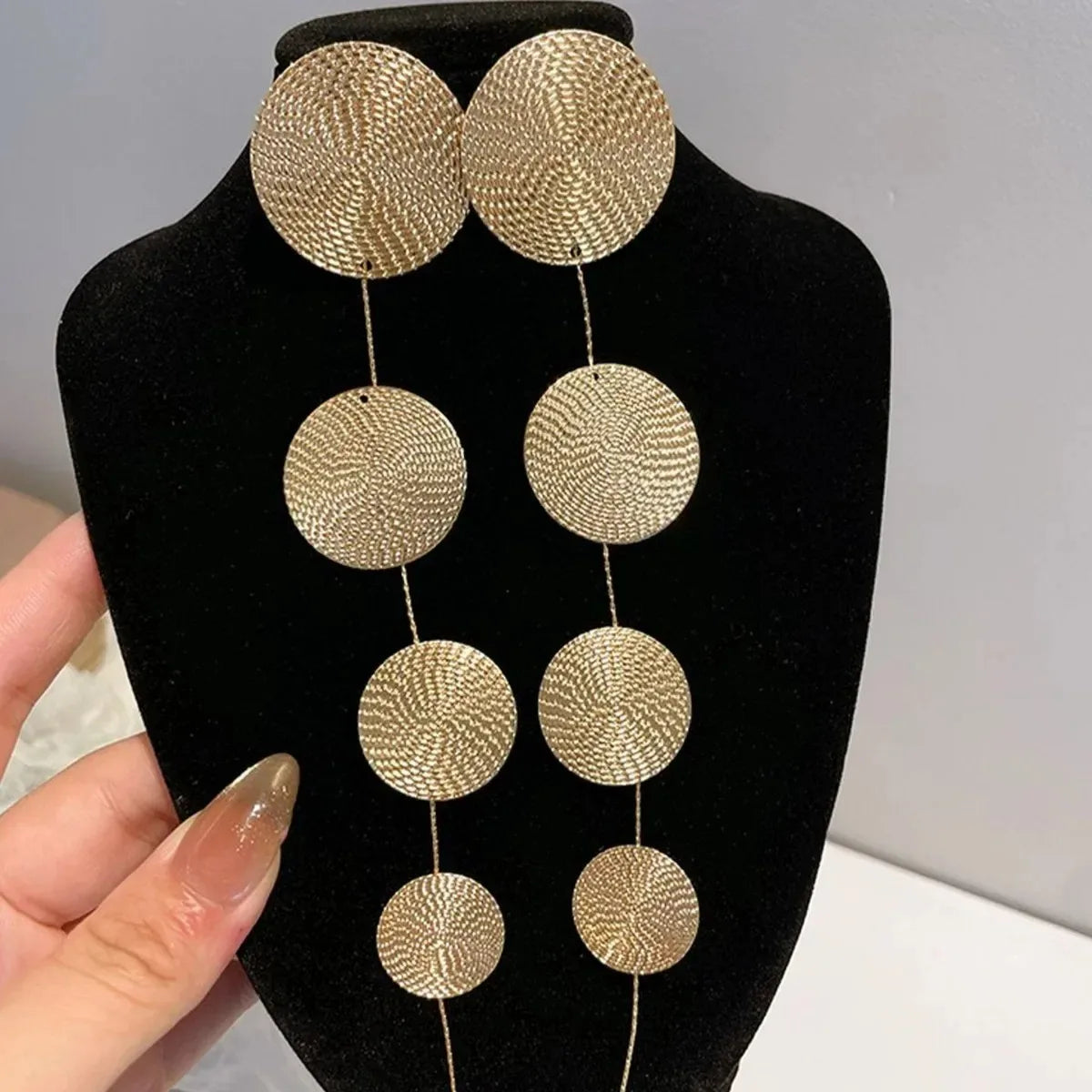 Gold-tone woven disc dangle earrings on black card, four-circle fringe drops