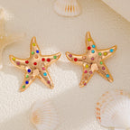 Gold starfish stud earrings with multicolor rhinestones, shown pair on seashells