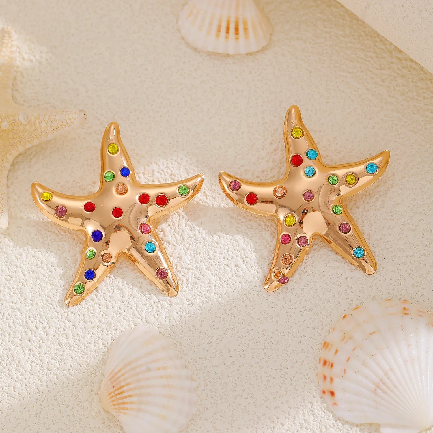 Gold starfish stud earrings with multicolor rhinestones, shown pair on seashells