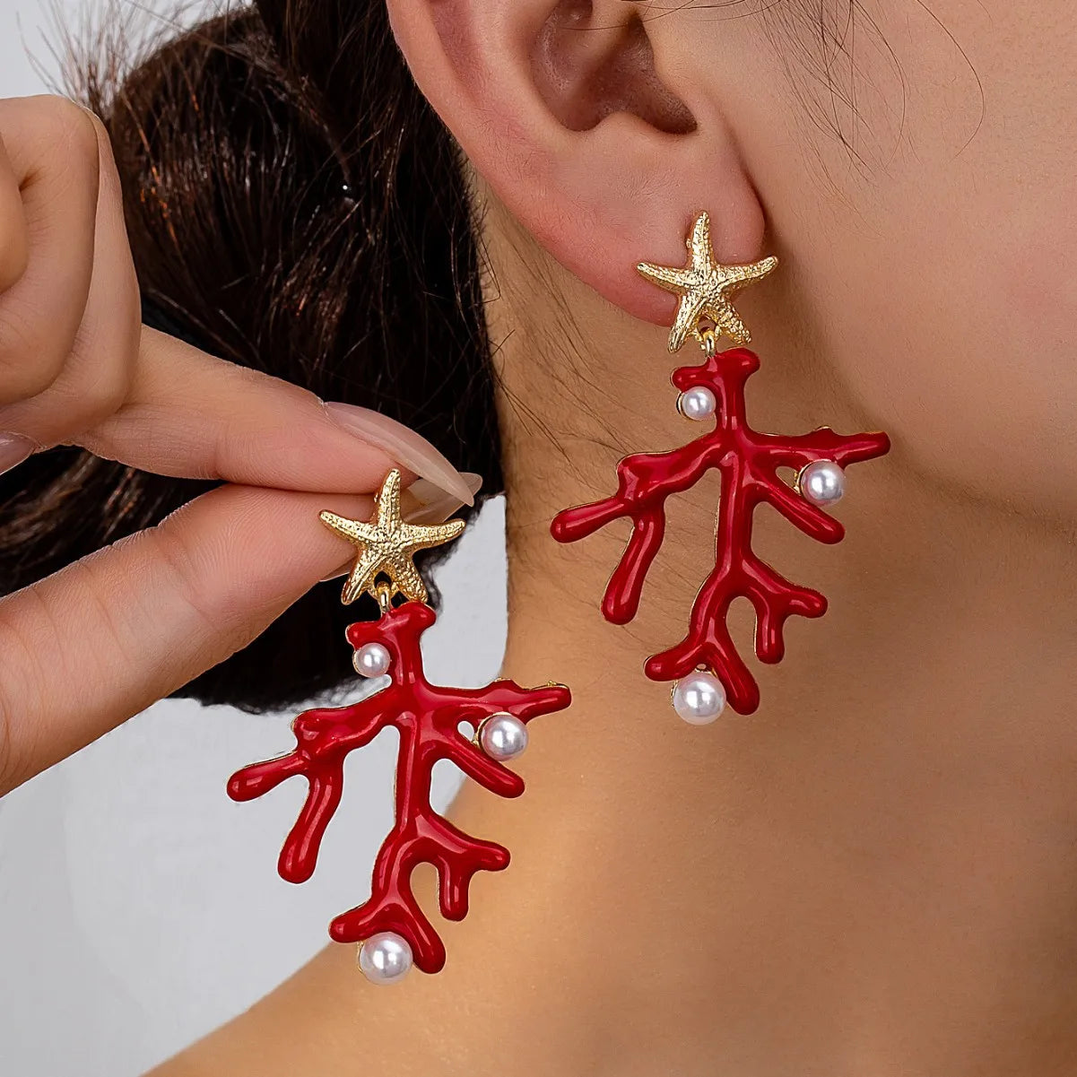 Starfish and coral earrings on ear: red enamel, gold-tone starfish, and pearl-like beads