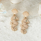 Gold-tone pearl shell earrings with teardrop tops and green jewel accents